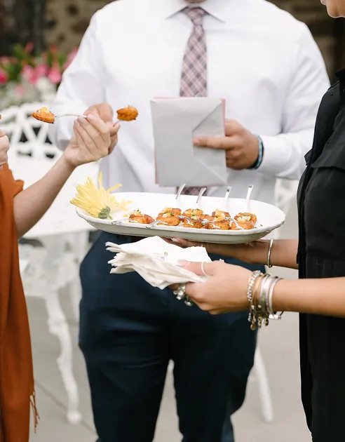 Server offering plated hors d'oeuvres to wedding guests outdoors