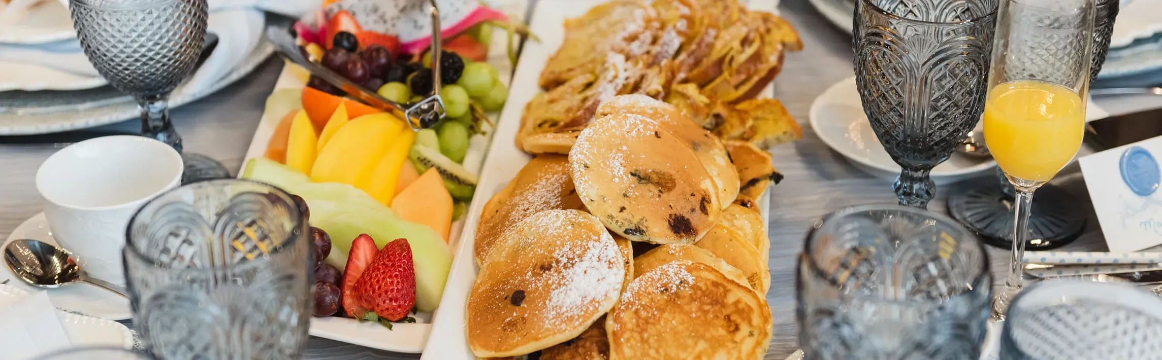 Brunch catering spread with pancakes, French toast, fresh fruit platter, and mimosa glassware