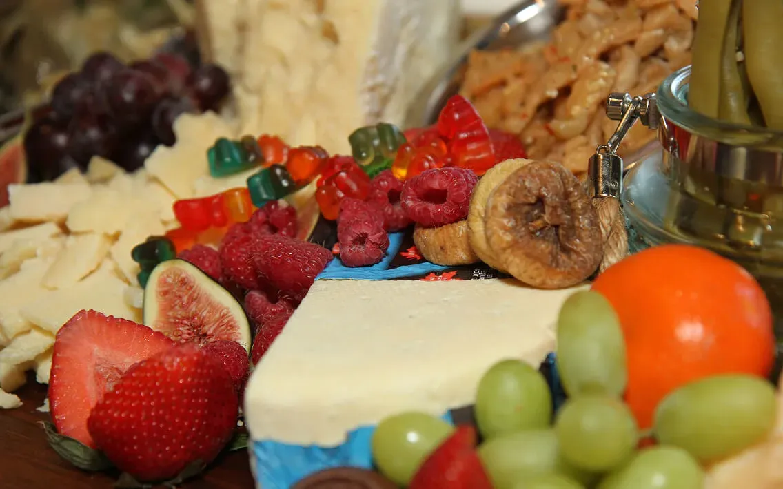 Close-up grazing board with strawberries, grapes, cheeses, figs, and colorful gummy bears