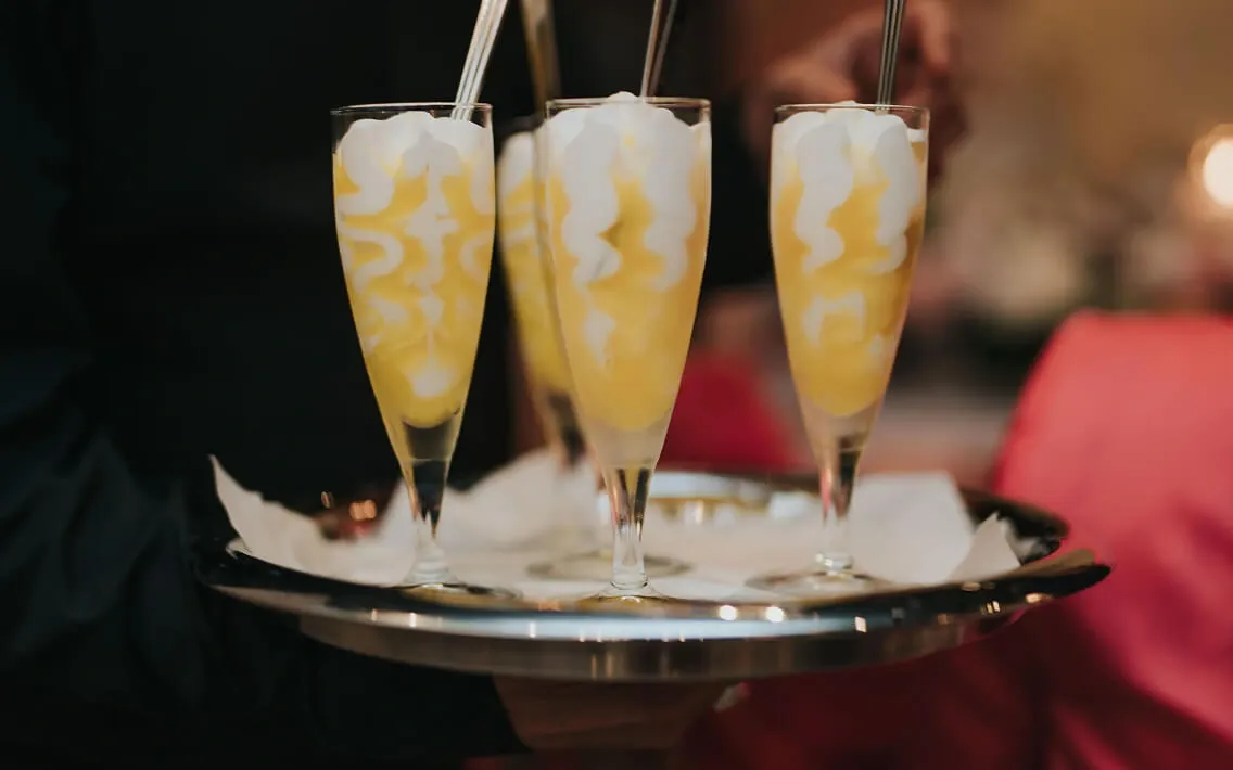 Server carrying a silver tray of stemmed lemon dessert glasses at a reception