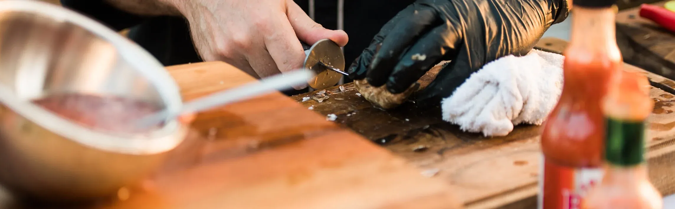 Chef in black coat shucking oysters beside a bowl of sauce at a live station