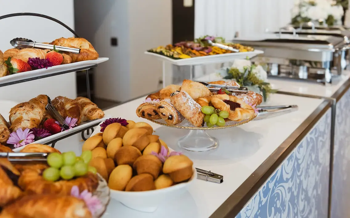 Breakfast buffet with croissants, muffins, pastries, and stainless chafing dishes