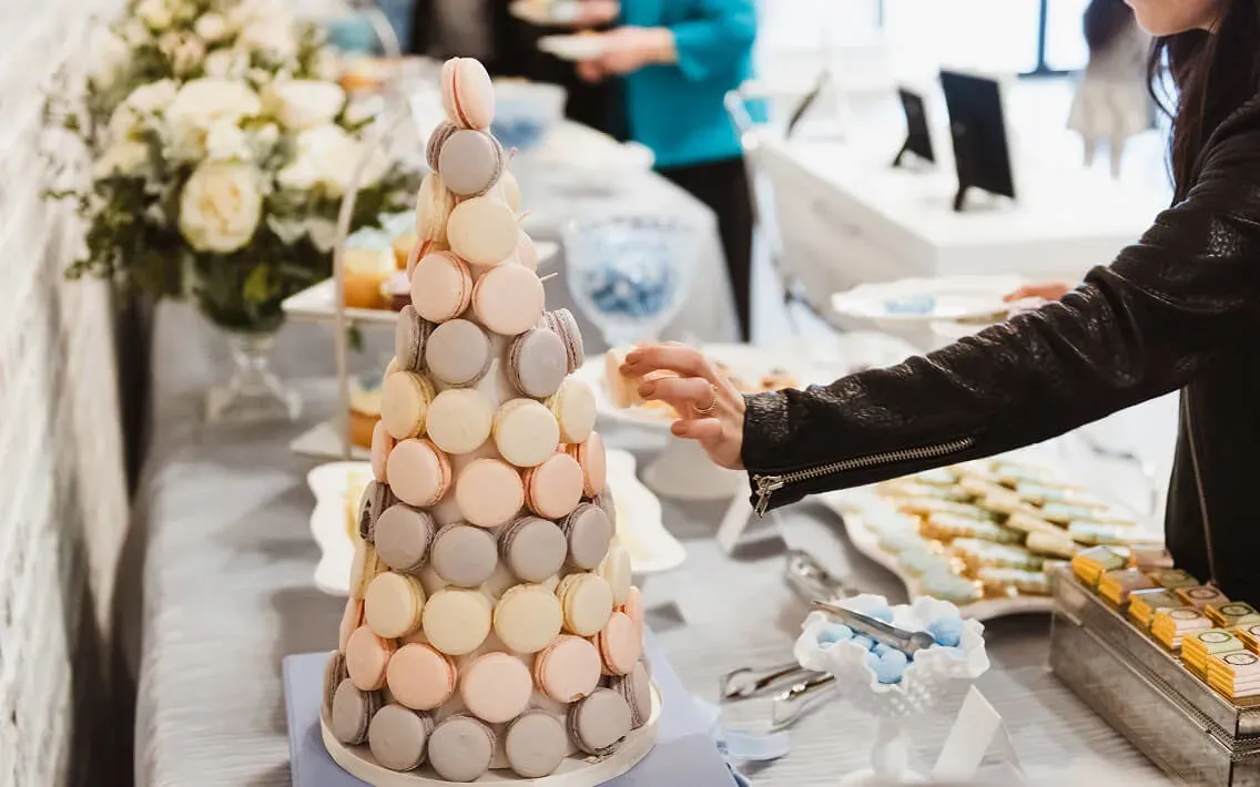 Pastel macaron tower on a dessert table as a guest reaches for a treat