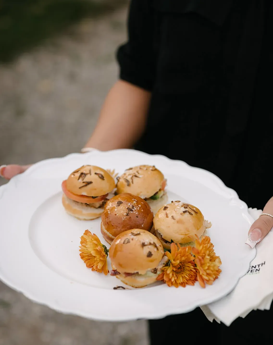 Server presenting mini brioche sliders garnished with orange blooms