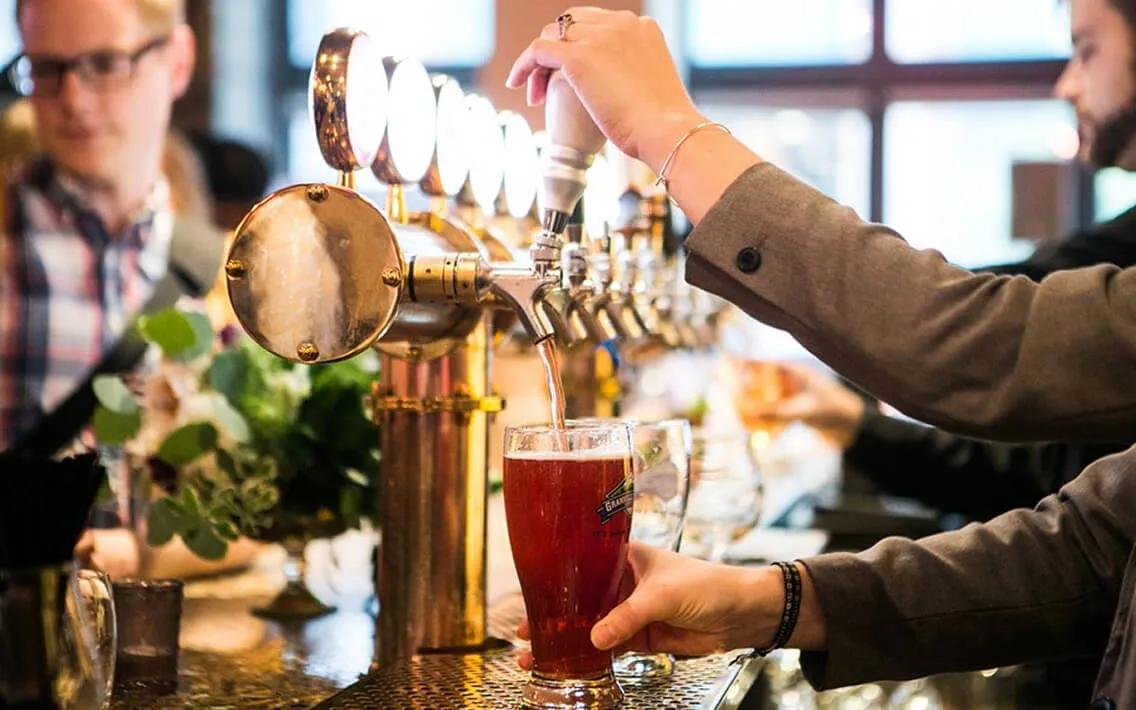 Bartender pouring amber beer from polished brass taps at a catered event bar