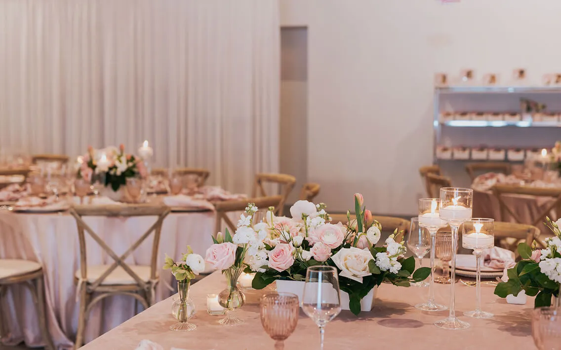 Blush-pink reception tables with rose centerpieces, floating candles, and cross-back chairs