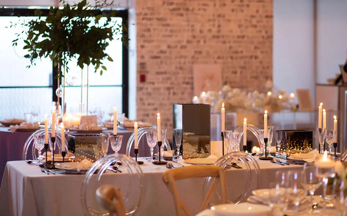 Long banquet table with lit white tapers, gold accents, and acrylic ghost chairs