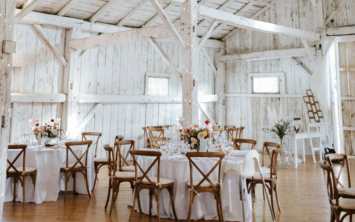 White barn reception with round tables, peach florals, taper candles, and string lights