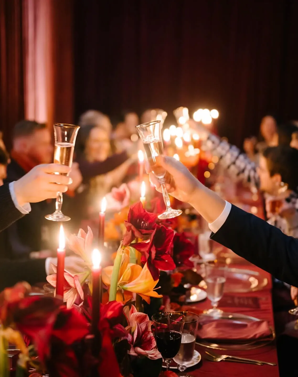 Guests clinking champagne flutes at a candlelit dinner with red amaryllis centerpieces