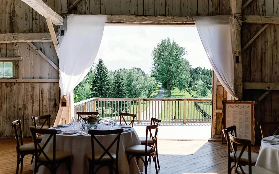 Barn reception tables facing open doors to a green outdoor landscape