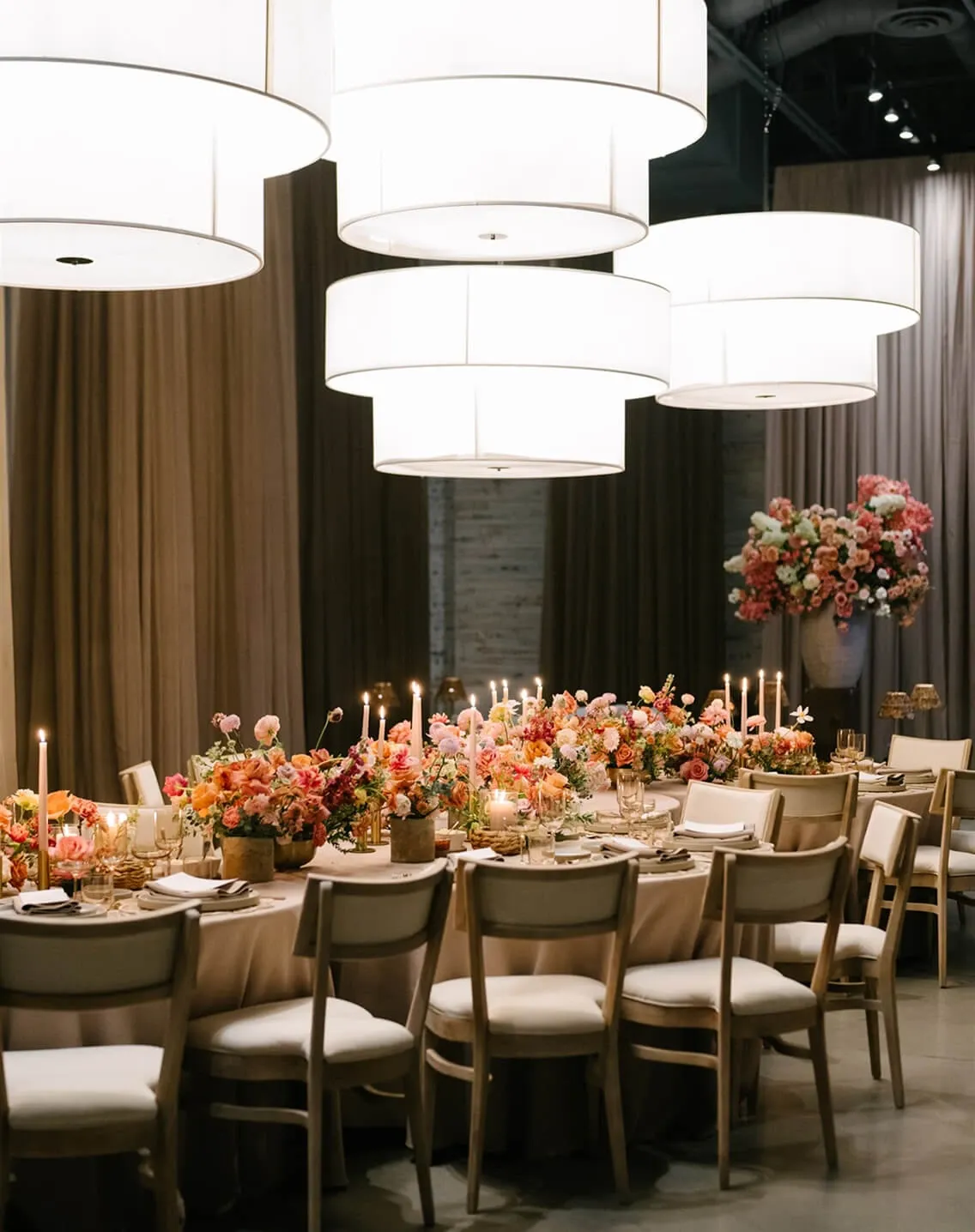 Long banquet table with peach floral runner, lit taper candles, and pendant lights