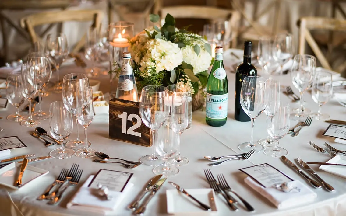 Round event table with hydrangea centerpiece, votives, printed menus, and Pellegrino