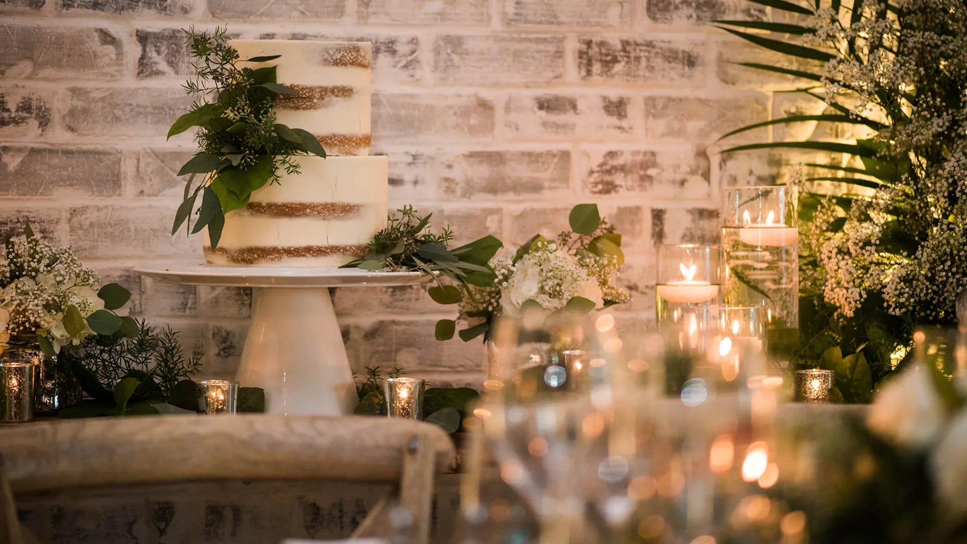 Two-tier semi-naked wedding cake with greenery and candlelight